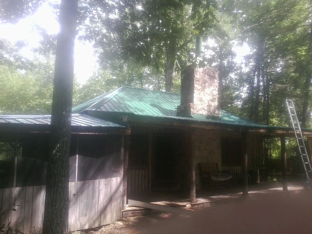 Green metal roof and stone chimney above a log cabin porch in Hollywood